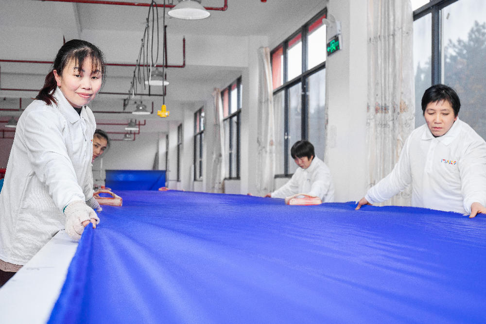Four female workers use the fabric puller to quickly unfold the fabric.
