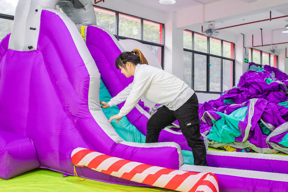 A worker carefully checks the appearance and sewing of the finished inflatable water slide.