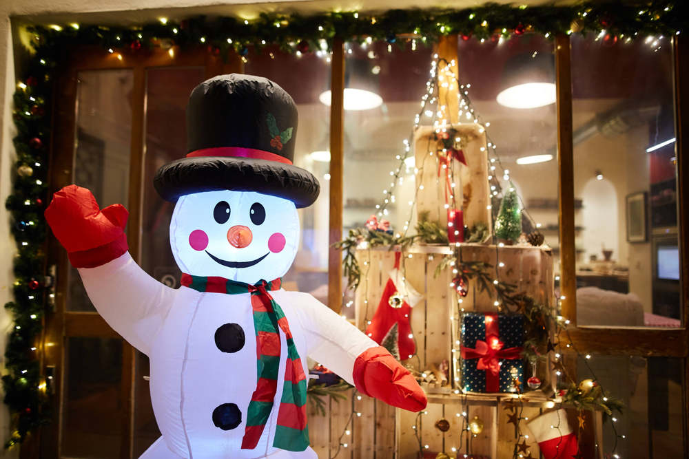 A store decorated with Christmas inflatable snowmen in front.