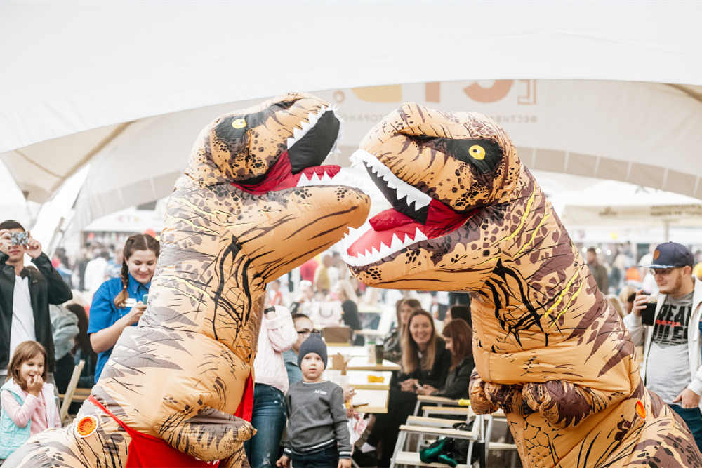 Two people wearing dinosaur inflatable clothes in the street.