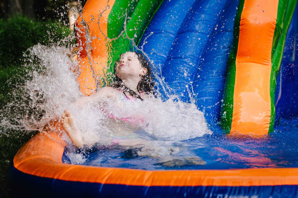 A little girl happily playing on the inflatable water slide.