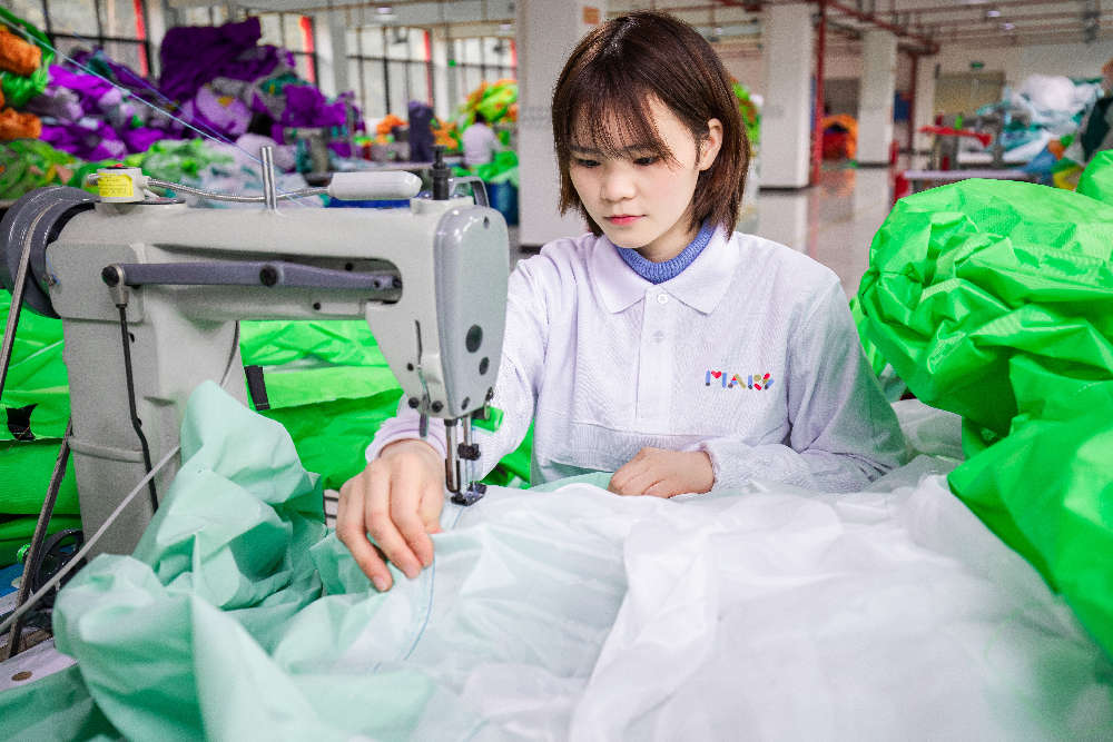A worker uses a sewing machine to sew bounce house products.